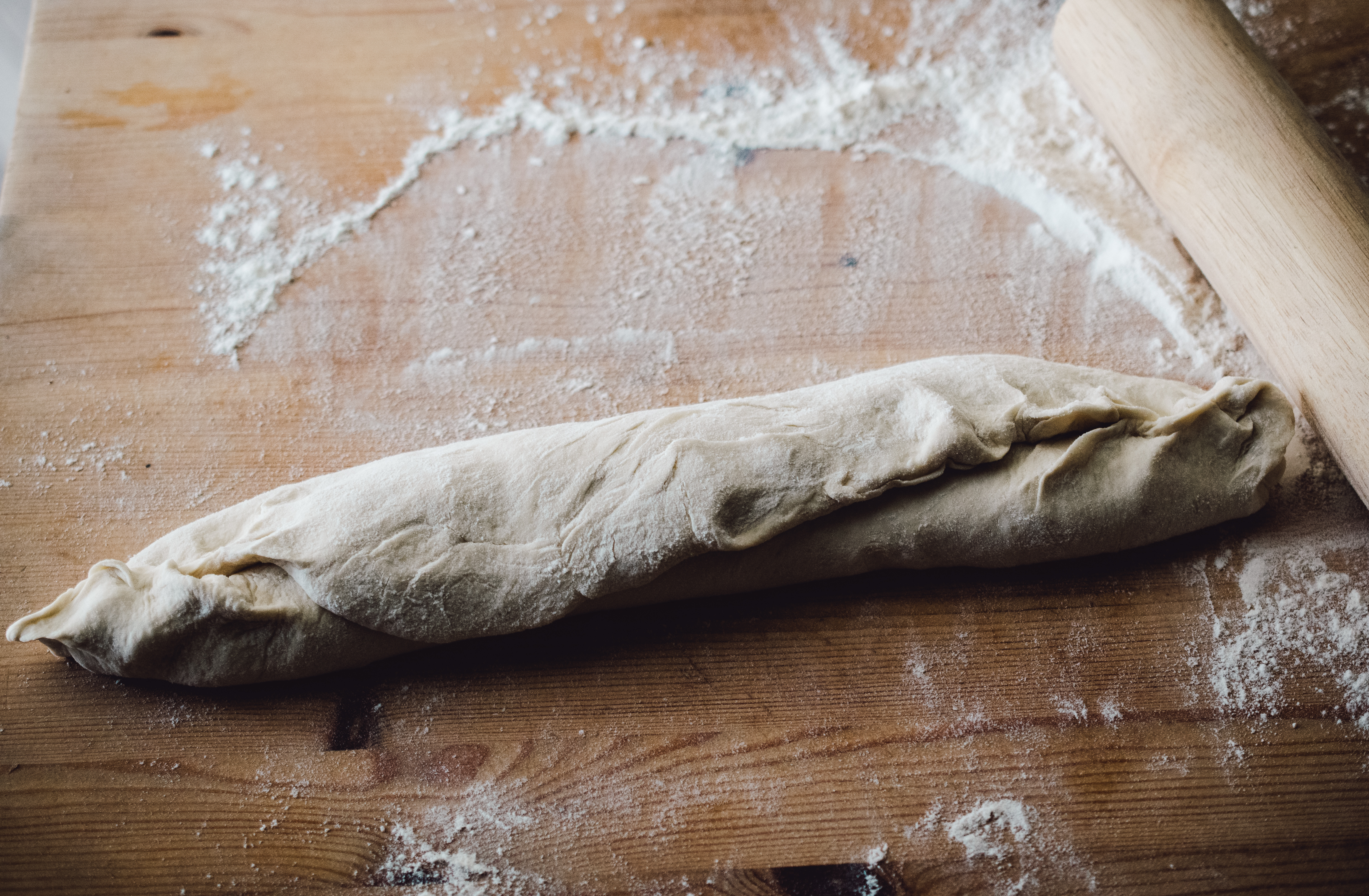 Raw, white bread dough, rolled into the classic French loaf shape, laying on a floured cutting board