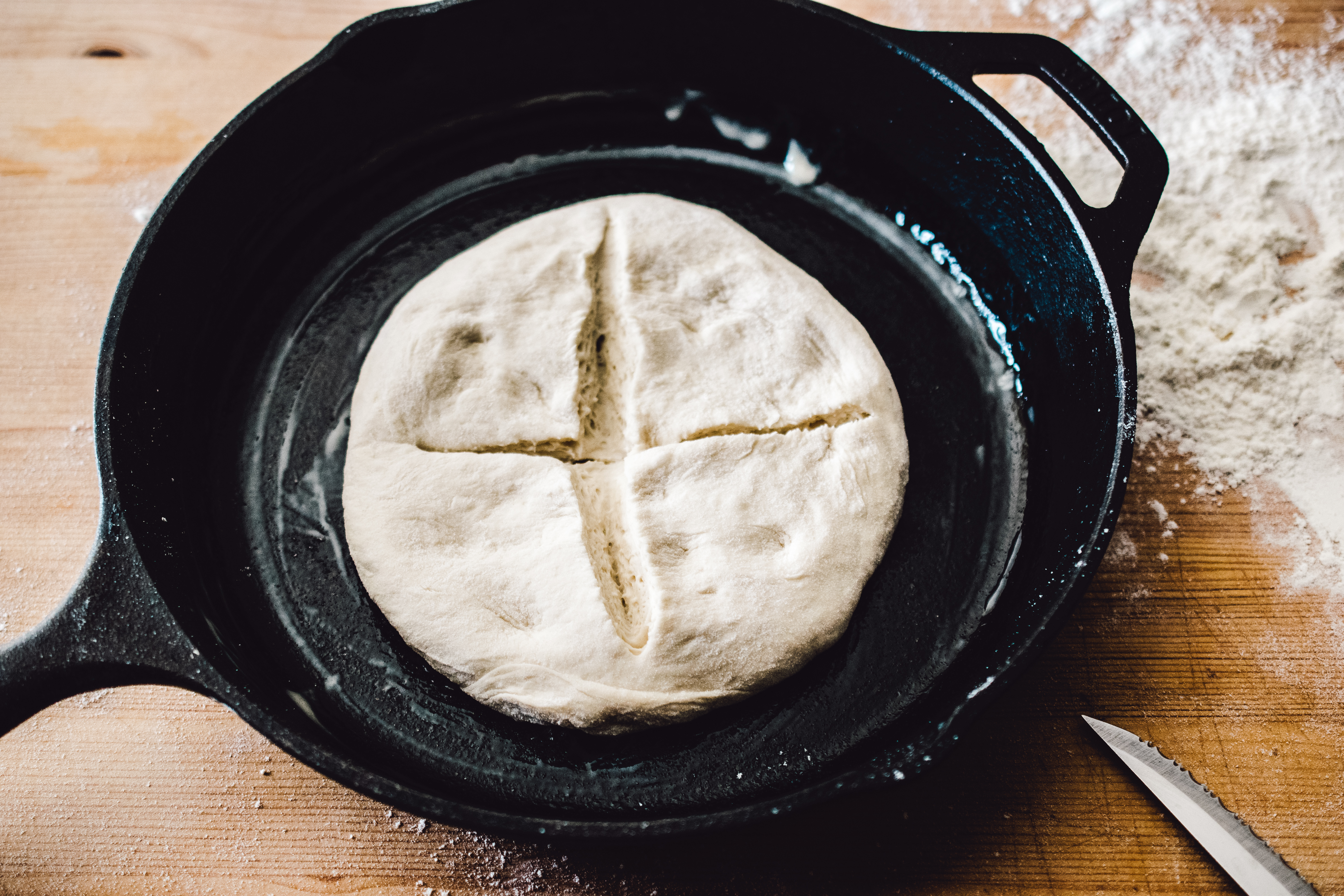 Homemade raw bread dough, formed into boule shape, laying in greased cast iron skillet, with an x slit in the top