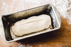 Raw white bread dough, shaped into a sandwich loaf, set in a greased, metal bread loaf pan and ready to rise and be baked