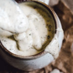 mug full of homemade ranch dressing and spoon dripping ranch dressing