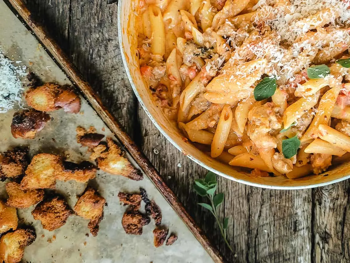 Pasta with vodka sauce and sausage in a skillet with rustic croutons.
