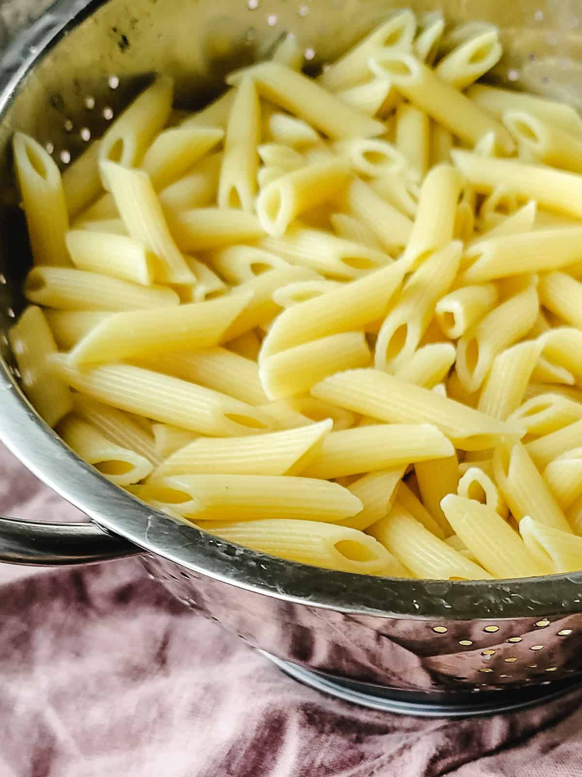 A steel strainer filled with cooked penne pasta.