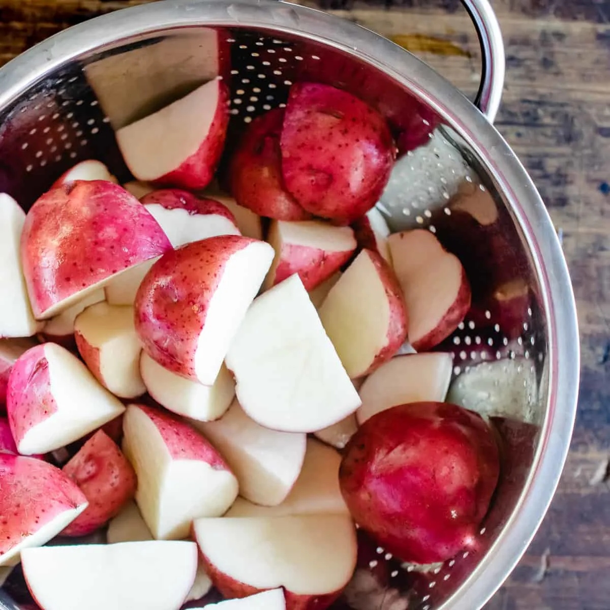 A strainer of rinsed and quartered red potatoes.