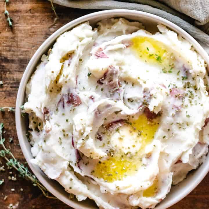 A large bowl of red skin mashed potatoes with butter and herbs.