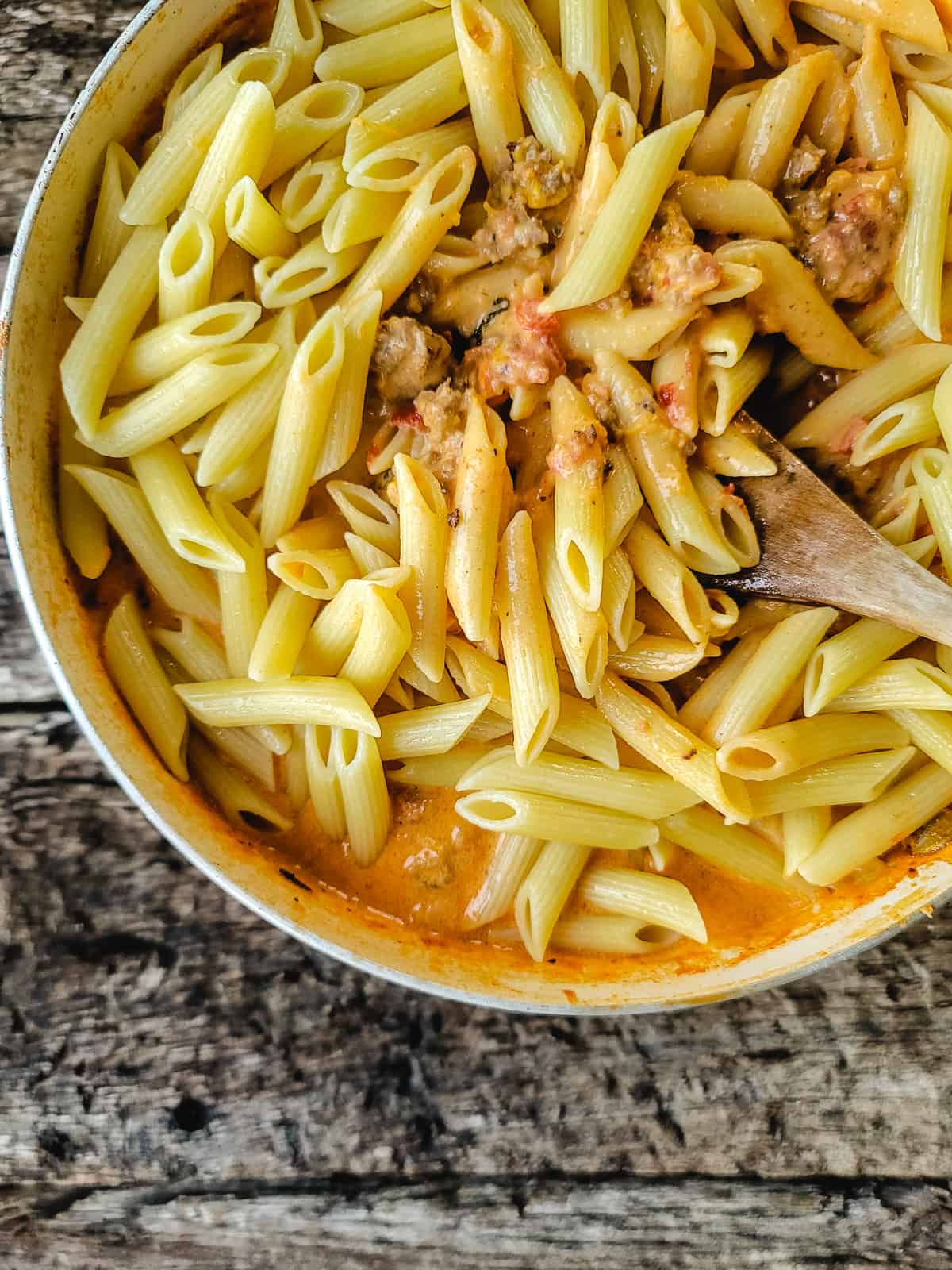 Penne pasta tossed in a tomato cream sauce in a skillet.