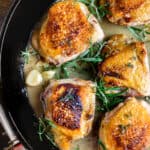 Skillet of browned chicken thighs with herbs and garlic in a sauce.