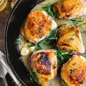 Seared chicken thighs in a cast iron pan with fresh herb sprigs and sauce.