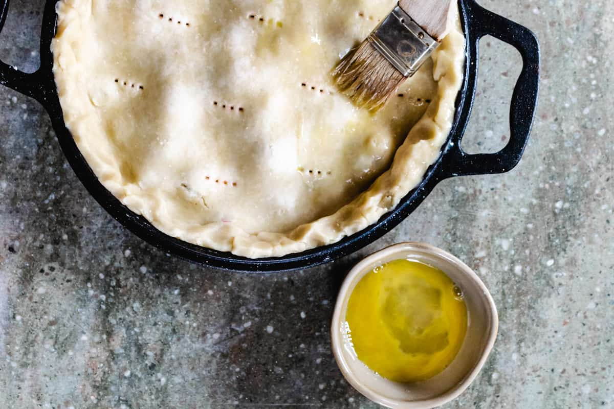 Brushing egg wash on the top of an unbaked pie.