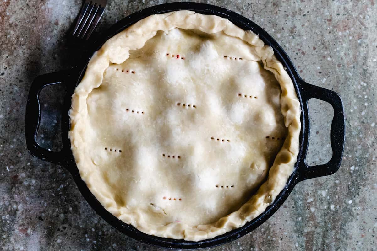 Cast iron pie pan with handles holding uncooked pie with holes poked in the top.