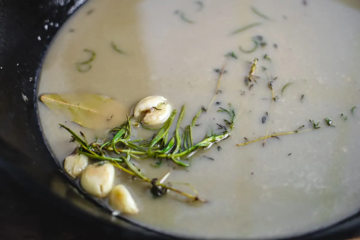 Sauce with herbs and garlic cloves in a cast iron skillet.