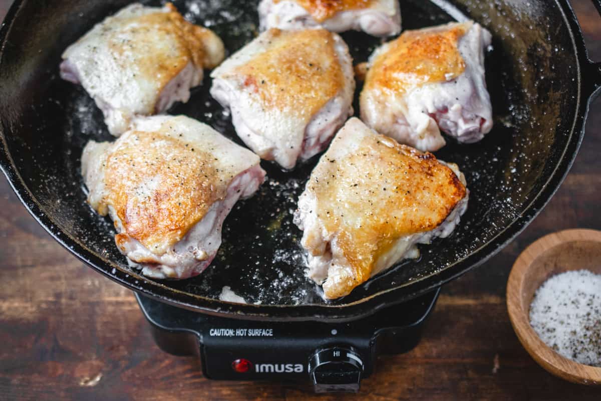 Chicken thighs being seared on a cast iron skillet.