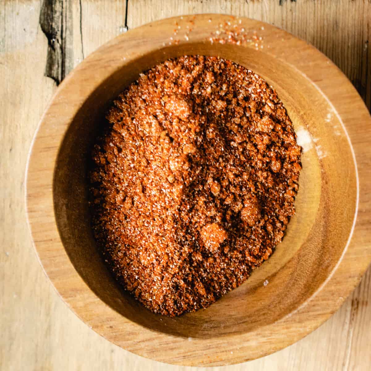 Wooden bowl of chili seasoning mixed up on a wooden cutting board.