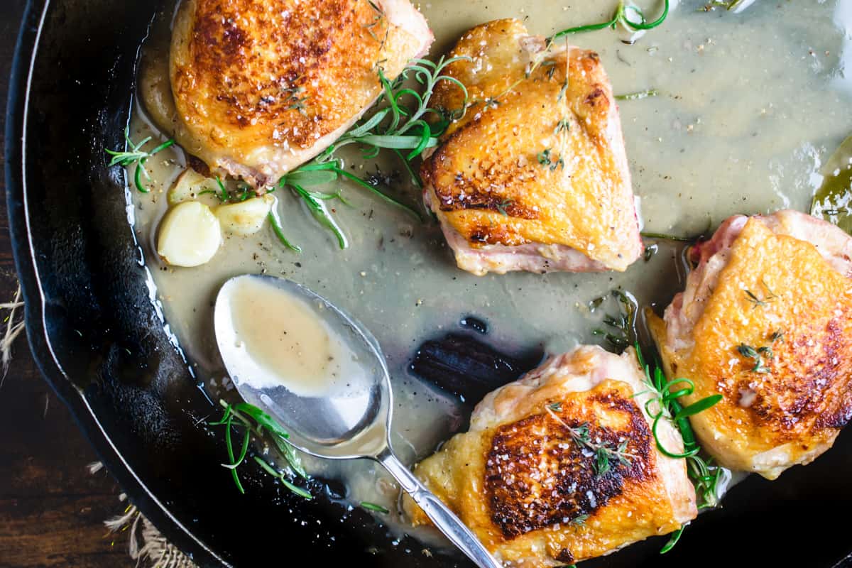 Crispy chicken thighs with herbs, spoon and sauce in a skillet.