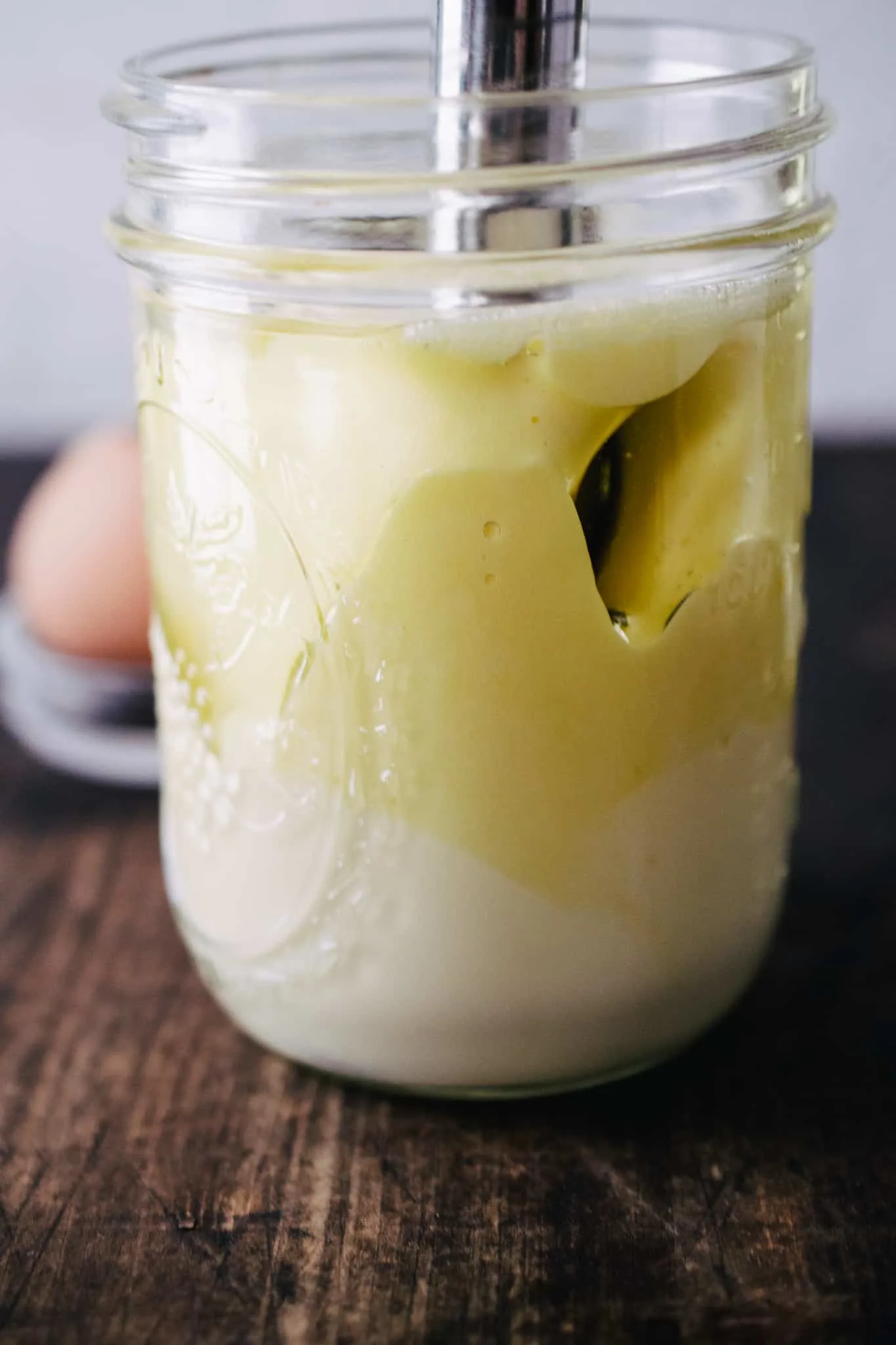 immersion blender in mason jar making homemade mayonnaise on dark wooden surface with white stone backdrop