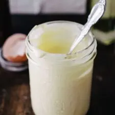 mason jar of homemade mayonnaise on wooden surface next to cracked egg shells