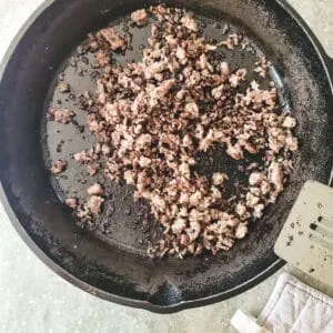 Ground pork frying in a cast iron skillet.