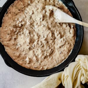 Cast iron skillet of country sausage gravy with wooden spoon