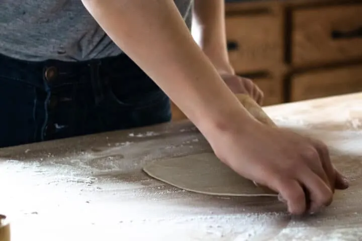 woman rolling out homemade tortillas on floured butcher block surface