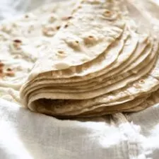 Stack of homemade flour tortillas folded in half on white cloth