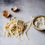 fresh fettuccine pasta with cracked brown egg and bowl of all purpose flour