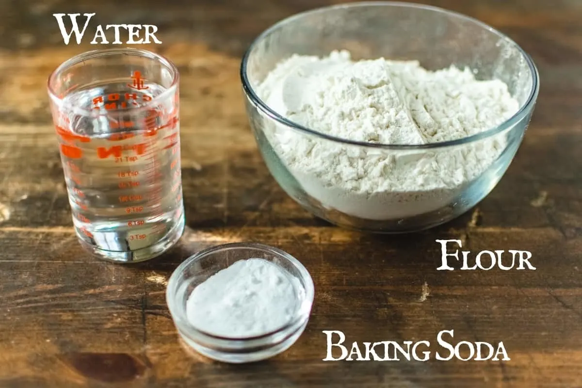 A bowl of flour, baking soda and cup of water on wooden surface.