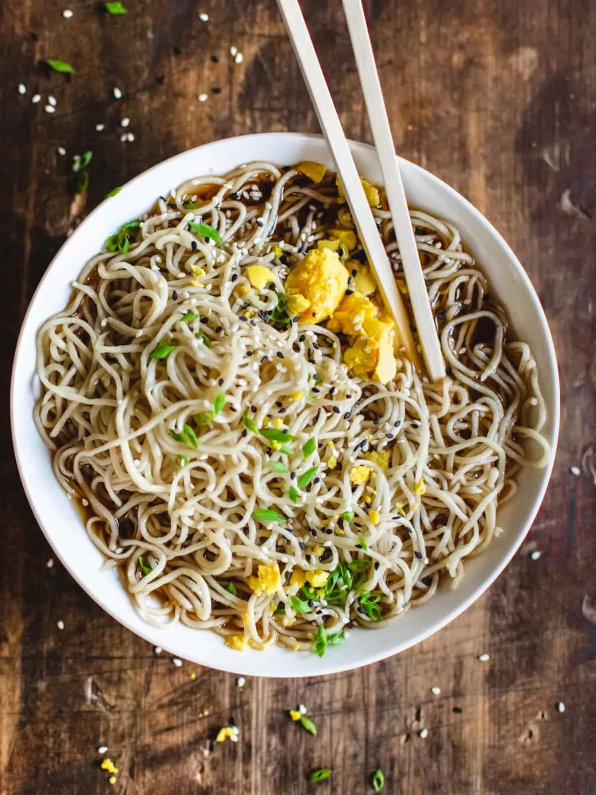 Bowl of ramen noodles in broth with egg yolk, scallions, sesame seeds and chopsticks.