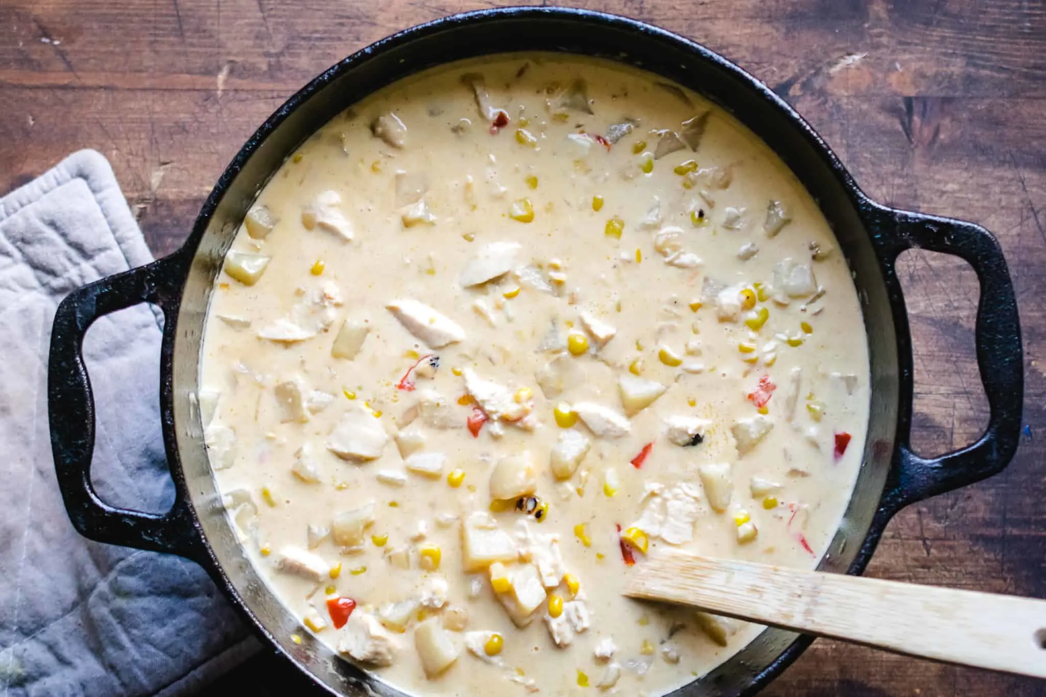 cast iron dutch oven full of creamy chicken and cheese corn chowder with wooden spoon