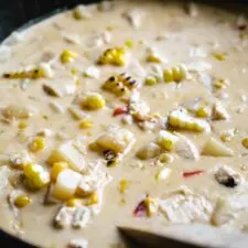 close up of cheesy chicken corn chowder with chunks of potato and red bell pepper and blackened corn cobs