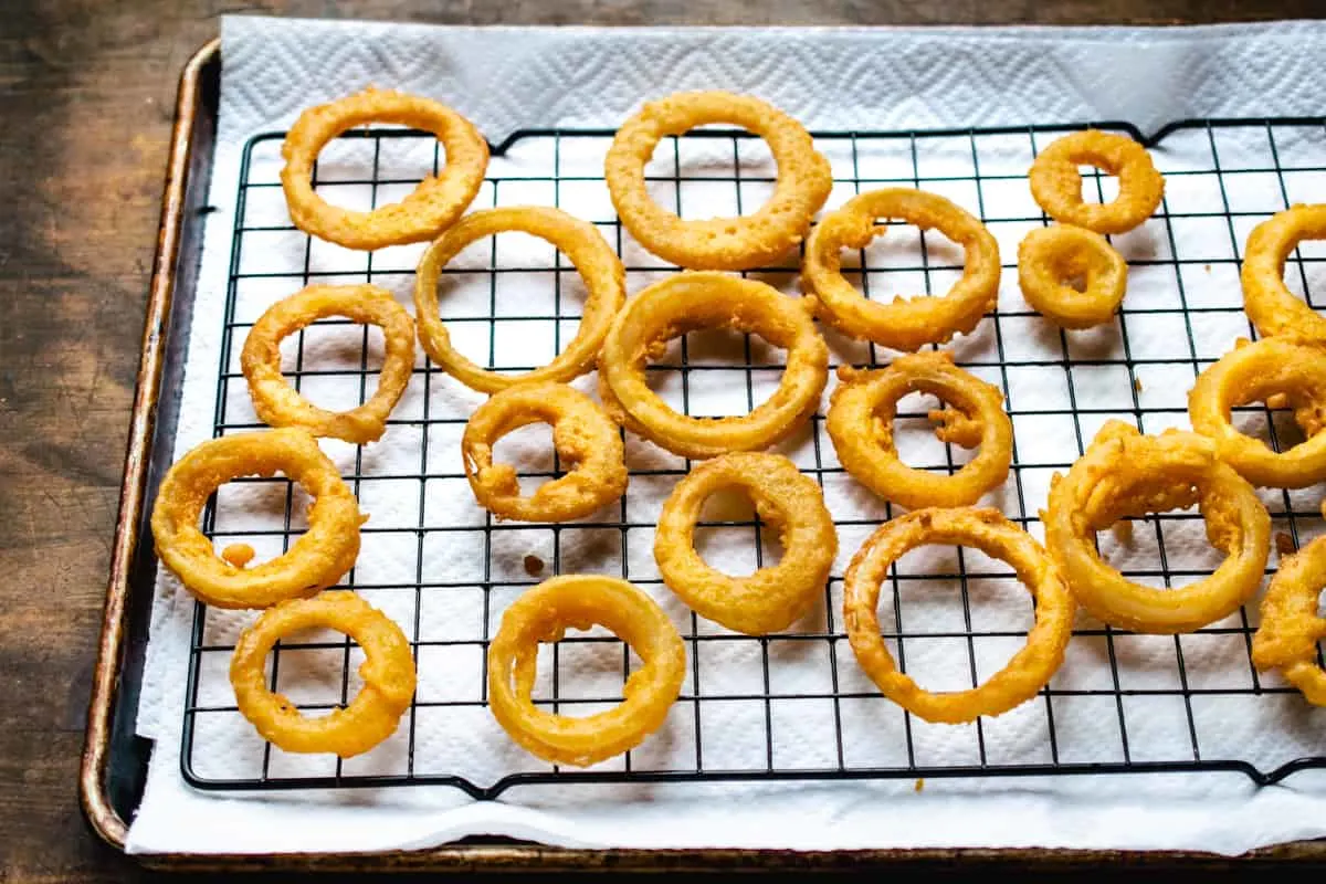 Fried onion rings on a black wire rack over paper towels on a baking sheet.