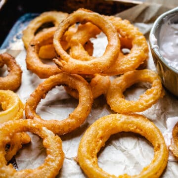 Breaded, fried onion rings on parchment paper with dipping sauce.