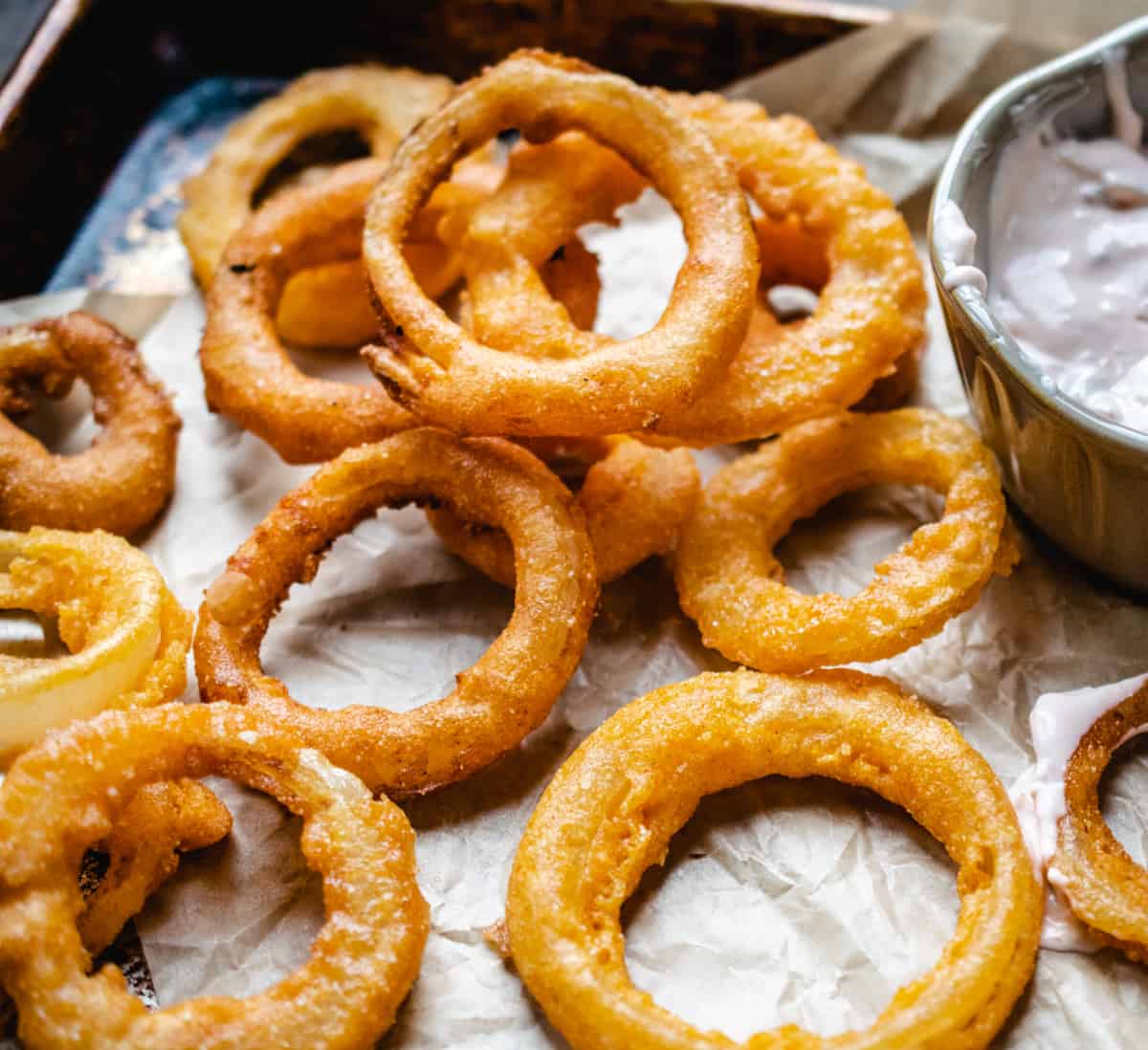 Breaded, fried onion rings on parchment paper with dipping sauce.