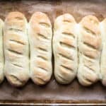 Hoagie bun rolls lined up on a baking sheet.