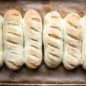 Hoagie bun rolls lined up on a baking sheet.