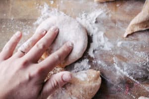 hand pressing dough into a burger bun shape on floured wooden surface