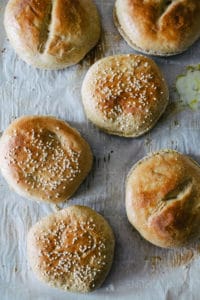 freshly baked split top and sesame seed hamburger buns on a parchment paper lined baking sheet