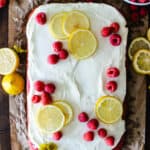 raspberry sheet cake on parchment paper topped with white frosting and fresh lemon slices and raspberries