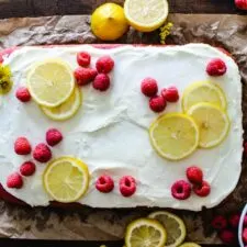 raspberry sheet cake with white frosting and fresh raspberries and lemon slices on brown parchment paper