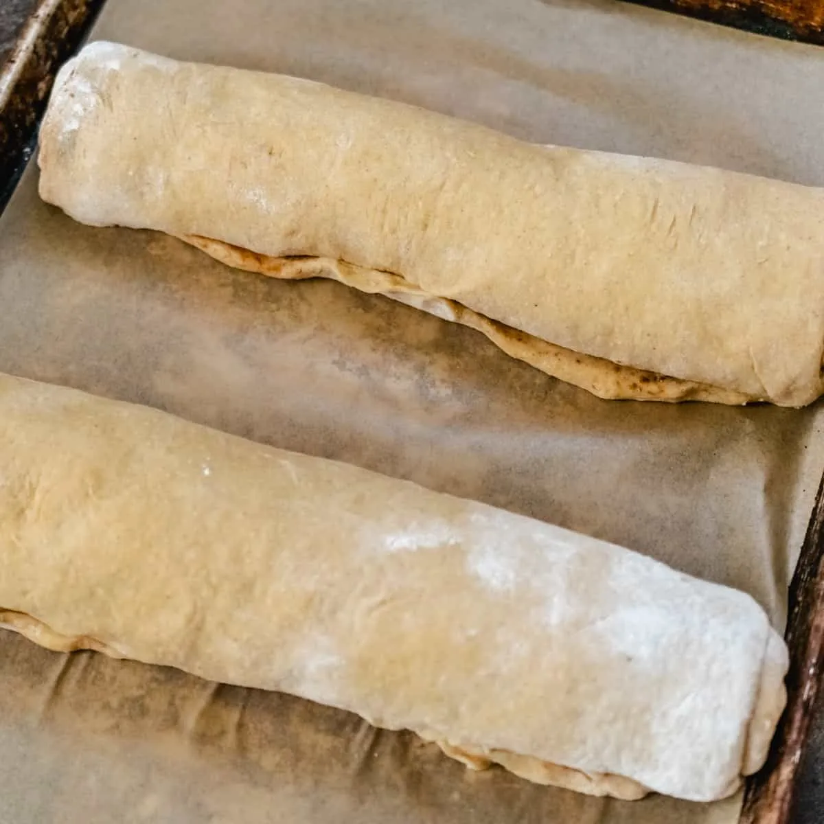 Two loaves of uncooked rolled up cinnamon dough on a baking sheet.