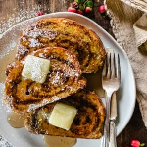 Three pieces of French toast on a plate with butter pads, syrup and powdered sugar.