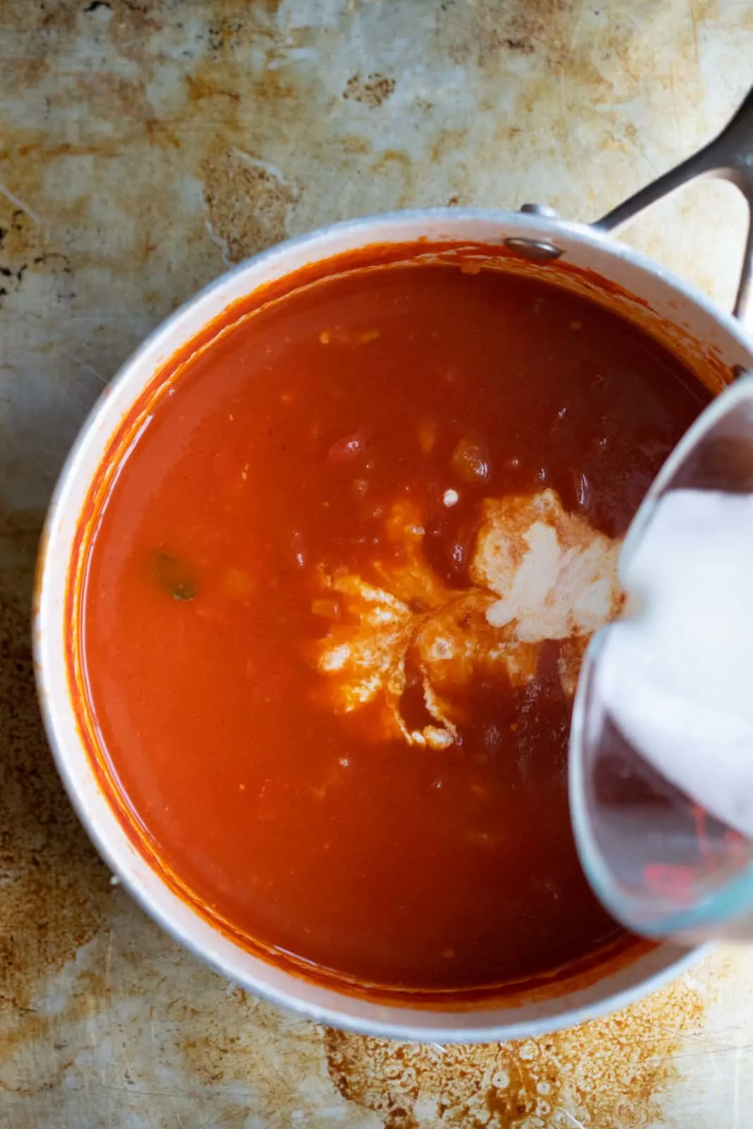 Cream being poured into a pot of homemade tomato and basil soup.