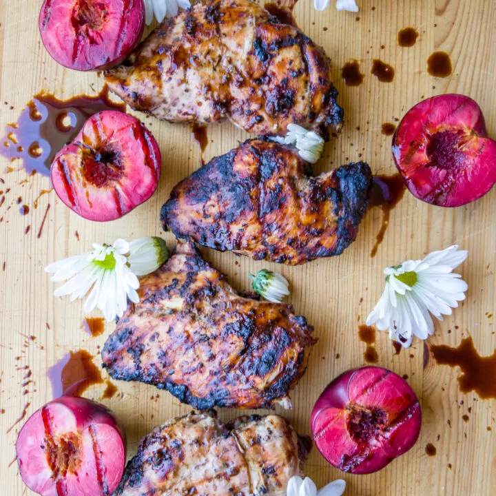 Chicken breasts with grilled plums and white flowers and sauce on a cutting board.
