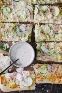 sliced homemade chicken ranch pizza with red onion and zucchini with ramekin of ranch dressing and fresh dill