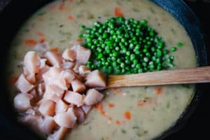 Skillet of creamy chicken and vegetable soup base for chicken and dumplings with raw diced chicken and peas added to be mixed