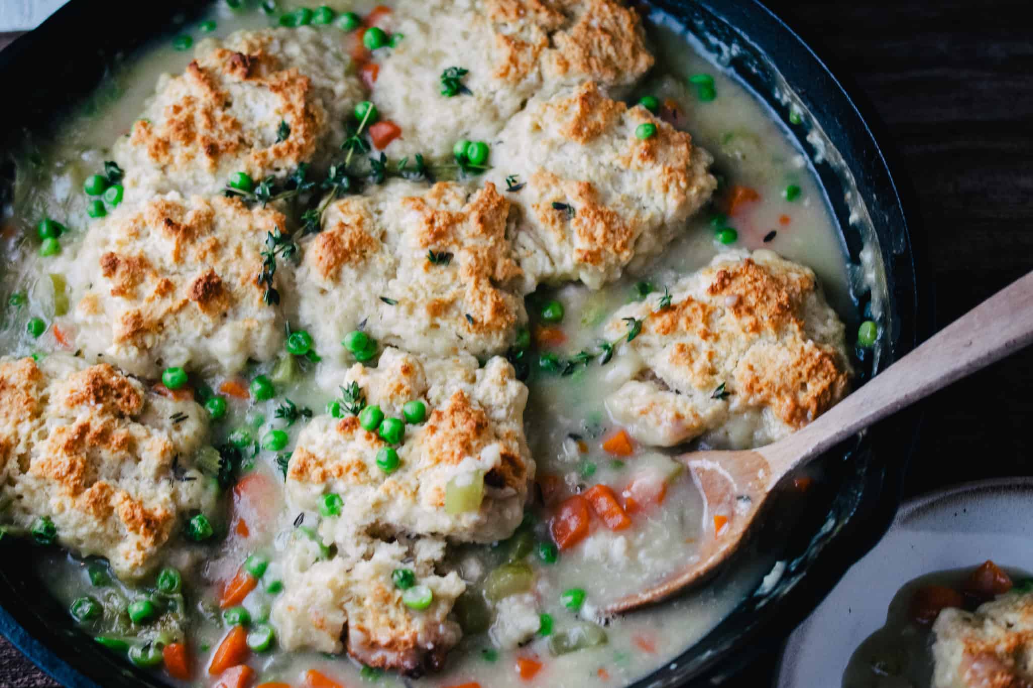 cast iron skillet filled with creamy chicken and dumplings with a wooden spoon on a wooden surface