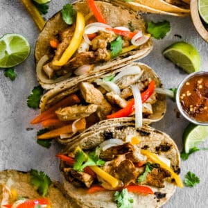 Fajita tacos arranged next to each other with lime wedges for serving.