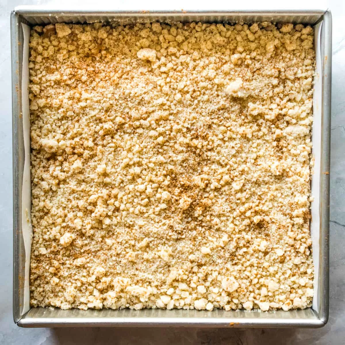 Cinnamon streusel topping over apple filling in a square pan. 