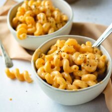 two white bowls of macaroni and cheese with black pepper on concrete background