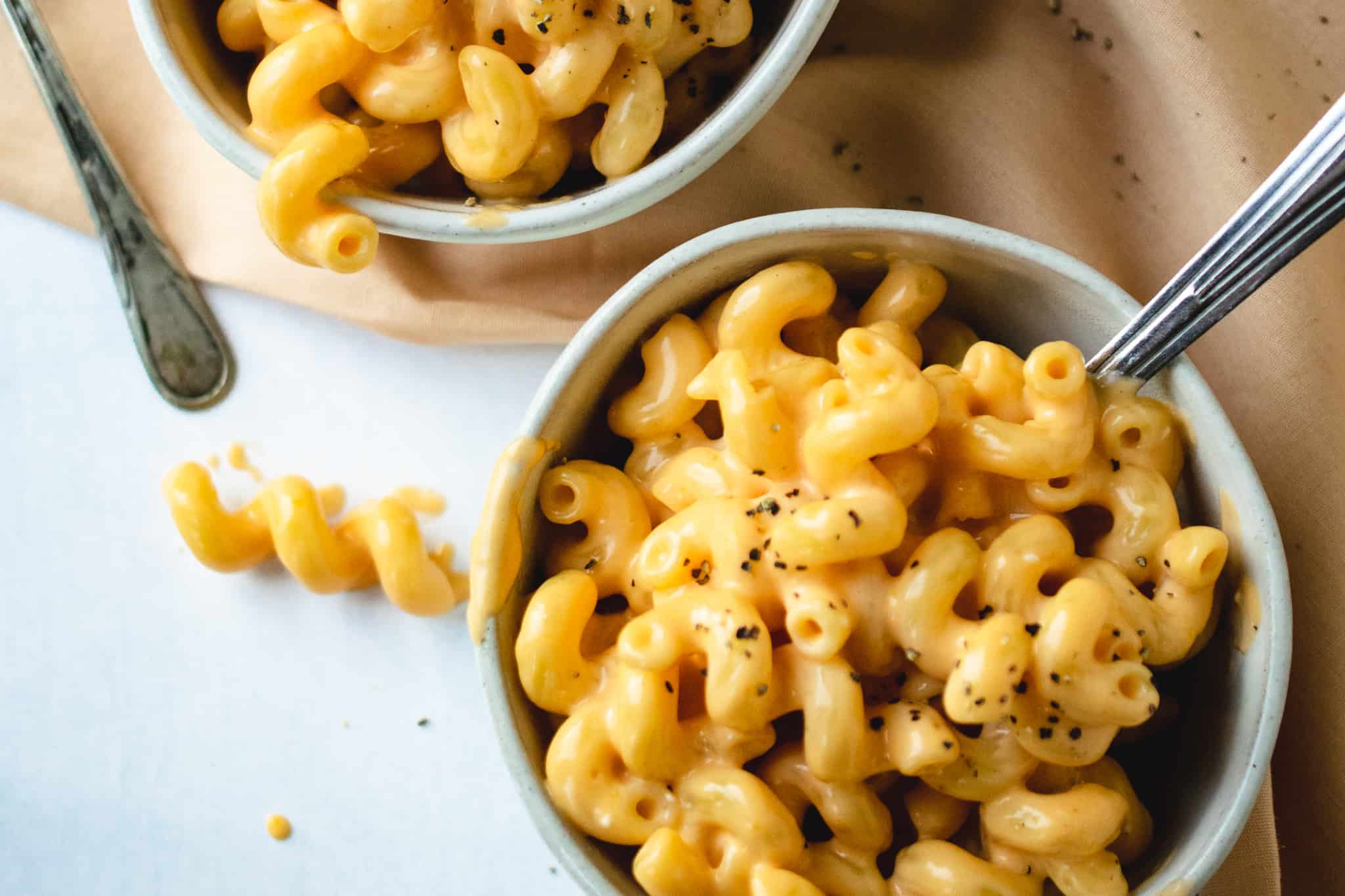 close up bowl of macaroni and cheese in white stoneware bowl with course ground black pepper on concrete background