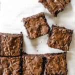brownie squares with crinkle tops cut into squares on white parchment paper and marble counter top