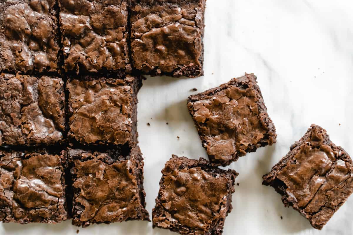brownies with shiny flaky tops cut into squares on white parchment paper